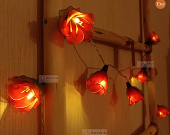 May include: String of fairy lights with red flower-shaped bulbs. The lights are strung on a wire and are lit up. The lights are hanging on a wooden ladder. The text "Marwin Craft" is visible on the image.