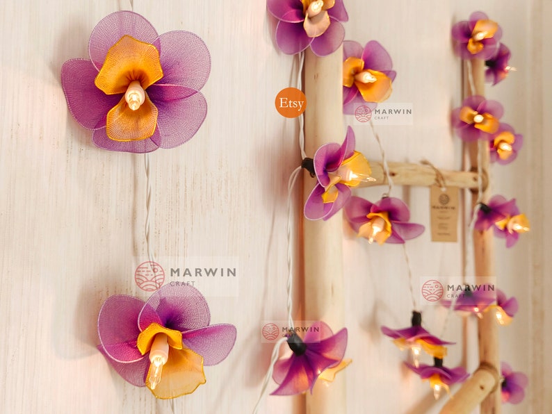 Puede incluir: Una cadena de luces con bombillas en forma de flor de color morado y naranja. Las luces est&aacute;n enhebradas en un cable blanco y est&aacute;n colgadas de una escalera de madera. El texto "Etsy" y "Marwin Craft" es visible en la imagen.