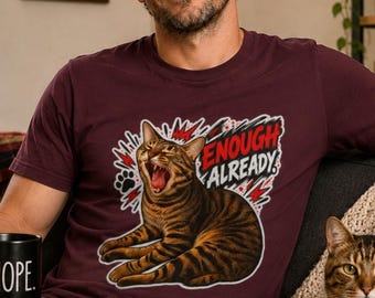 May include: A maroon short-sleeved t-shirt featuring a graphic of a yawning brown tabby cat with black stripes. The design includes red lightning bolt accents, a black paw print, and the text "ENOUGH ALREADY" in bold white and red lettering.