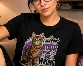 May include: A black short-sleeved t-shirt featuring a graphic of a brown tabby cat wearing a pink collar. The design includes a purple circular background with stars and the text I SUPPORT YOUR RIGHT TO BE WRONG in white and purple lettering.