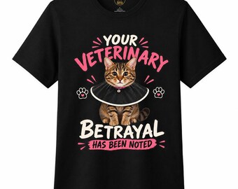 May include: A black short-sleeved t-shirt featuring a graphic of a brown tabby cat wearing a black cone collar. The text reads YOUR VETERINARY BETRAYAL HAS BEEN NOTED in pink and white lettering, accented by small white paw print icons.