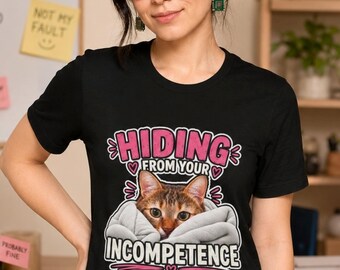May include: A black short-sleeved t-shirt featuring a graphic of a brown tabby cat peeking out from a grey blanket. The text reads HIDING FROM YOUR INCOMPETENCE in pink and white lettering, accented with small pink hearts and decorative lines.