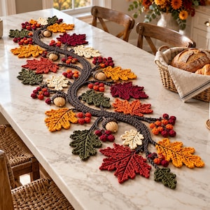 May include: A long, decorative crochet table runner featuring a central dark brown vine-like structure adorned with various autumn-themed elements, including crocheted maple and oak leaves in shades of red, orange, yellow, and green, plus small berries.