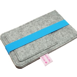 May include: Grey felt phone case with a blue elastic band and a pink label that says "artista lista".
