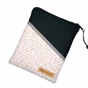 Könnte beinhalten: Eine schwarze und graue Reißverschlusstasche mit einem weißen Stofffutter, das ein handschriftliches Skriptmuster aufweist. Die Tasche hat ein kleines braunes Etikett mit dem aufgedruckten Wort "artistalista".