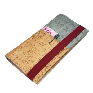 Könnte beinhalten: Eine Brieftasche aus Kork und Filz mit einem roten Bandverschluss. Die Brieftasche hat ein Fach für einen Stift und einen Kartensteckplatz.