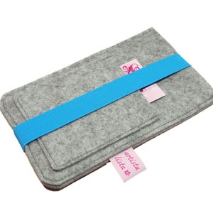 May include: Grey felt phone case with a blue elastic band and a pink label that says "artista lista".