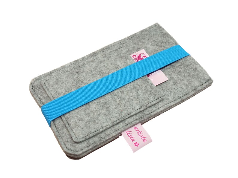 May include: Grey felt phone case with a blue elastic band and a pink label that says "artista lista".