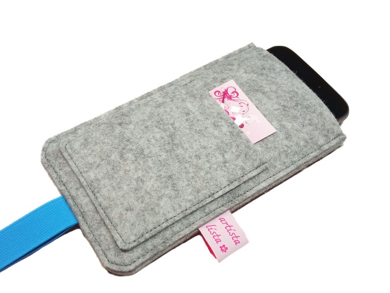 May include: Grey felt phone case with a blue strap and a pink pocket with the text "artista lista" on it.