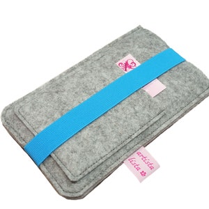 May include: Grey felt phone case with a blue elastic band and a pink label that says "artista lista".