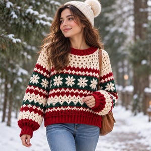 Può includere: Un maglione all'uncinetto a maniche lunghe con un motivo ripetuto di strisce orizzontali color crema, verde scuro e rosso con disegni di fiocchi di neve bianchi. Il maglione presenta un girocollo, polsini a coste e un orlo a coste.