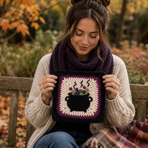 May include: A square crochet patch featuring a black cauldron graphic with green and purple bubbles and rising steam. The design is framed by a cream-colored border and an outer black border, creating a distinct square shape with textured yarn.