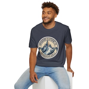 May include: A dark blue short-sleeve t-shirt featuring a circular graphic on the chest. The graphic depicts a mountain range with snow-capped peaks, surrounded by a rope-style border and the text WAYBOUND CLOTHING CO. THE MOUNTAIN CALLS.