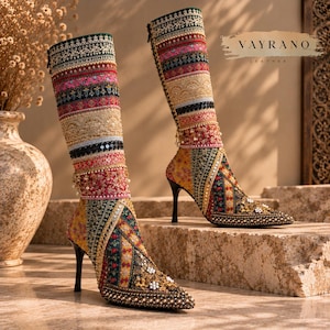 Puede incluir: Un par de botas altas de tacón de aguja con la marca VAYRANO LEATHER. Las botas están decoradas con paneles de tela bordada multicolor, abalorios intrincados, lentejuelas y pequeñas perlas blancas en un diseño de patchwork.