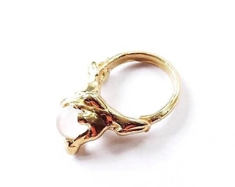 May include: A gold ring featuring a white stone set in a distinctive, organic design. The ring is crafted from textured metal and has a delicate, feminine feel.