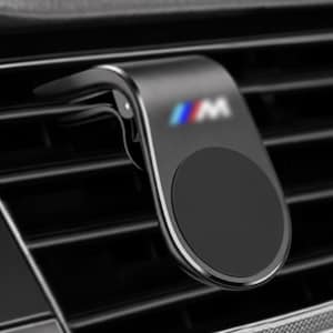 May include: A matte black magnetic car phone mount featuring a curved arm and a circular magnetic pad. The mount is attached to a horizontal vehicle air vent and displays a small, blurred M logo with blue, purple, and red color accents.