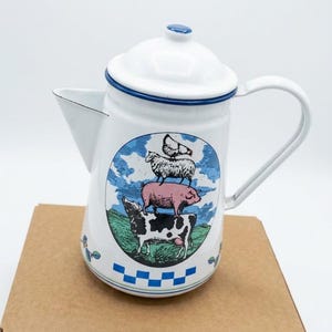 Puede incluir: Una cafetera de esmalte blanco con borde y pomo de tapa azules. El frente presenta una ilustración circular de una vaca, un cerdo, una oveja y un pollo apilados en un campo. Un patrón de cuadros azul y blanco bordea la base de la cafetera.