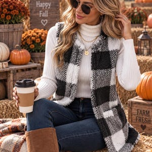May include: A sleeveless vest featuring a black and white buffalo plaid pattern made of a textured, fuzzy material. The vest is worn over a white ribbed turtleneck long-sleeve shirt, paired with dark blue denim jeans and brown knee-high boots.