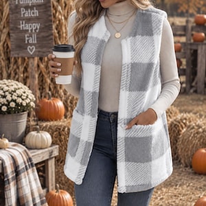 May include: A sleeveless vest featuring a white and grey buffalo plaid pattern made of a soft, fuzzy material. The vest has an open front design with two large patch pockets on the lower front panels and a straight hemline that reaches the hips.