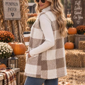 May include: A sleeveless vest featuring a cream and tan buffalo plaid pattern made of a textured, fuzzy fleece material. The vest has a straight hemline, side pockets, and is worn over a white long-sleeved ribbed turtleneck shirt and blue jeans.