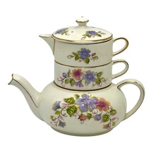 May include: A cream-coloured ceramic tea set for one, featuring a stacked teapot and teacup with gold-trimmed edges. The set is decorated with hand-painted purple and orange floral motifs, green leaves, and delicate vines on both pieces.