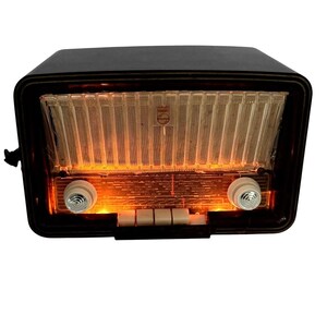 May include: A vintage Philips radio with a black rectangular casing and a glowing orange illuminated dial. The front features a clear ribbed speaker grille, two round white control knobs on the sides, and four rectangular white push buttons below.