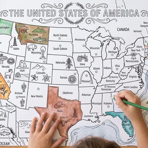 May include: A large, black and white printed map of the United States of America with some states partially colored in. The map features state names, capital cities, and various regional illustrations like animals, plants, and landmarks. A hand holds a green pencil.