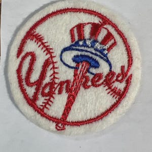 May include: A circular white embroidered patch featuring a red baseball stitch pattern and the word Yankees in red script. A blue and red top hat icon sits atop a red baseball bat. A measuring tape shows the patch is approximately 2 inches wide.