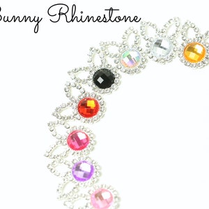 May include: Assortment of colorful rhinestone embellishments with silver settings. The rhinestones are in various colors, including red, pink, purple, blue, black, orange, and clear.