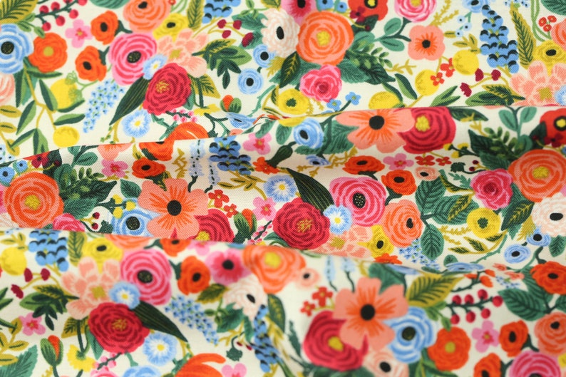 May include: Fabric featuring a vibrant floral design on a cream background. The pattern includes red, pink, orange, and blue flowers, alongside green foliage. The flowers are densely packed across the fabric's surface.
