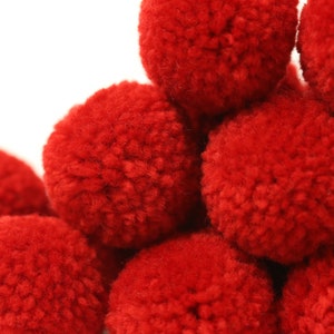 May include: A group of red pom-poms arranged in a pyramid shape. The pom-poms are made of soft, fluffy yarn.