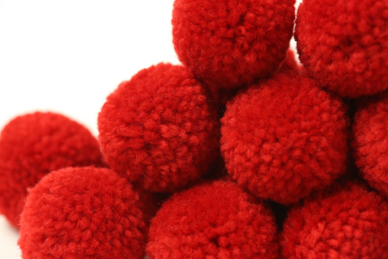 May include: A group of red pom-poms arranged in a pyramid shape. The pom-poms are made of soft, fluffy yarn.