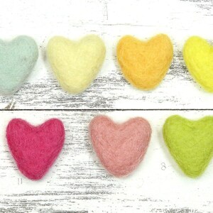 Puede incluir: Surtido de 16 corazones de fieltro en varios colores, incluyendo rojo, rosa, azul, verde, amarillo, naranja, blanco, negro y gris. Los corazones est&aacute;n dispuestos en dos filas sobre un fondo de madera blanca.