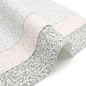 May include: Three rolls of white fabric with different floral patterns. The top roll has a light blue floral pattern, the middle roll has a light pink floral pattern, and the bottom roll has a black floral pattern.
