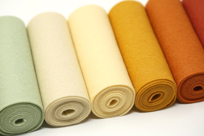 Puede incluir: Seis rollos de fieltro en varios tonos de verde, crema, amarillo, naranja y rojo. Los rollos est&aacute;n dispuestos en una fila de izquierda a derecha, con el rollo verde a la izquierda y el rollo rojo a la derecha.