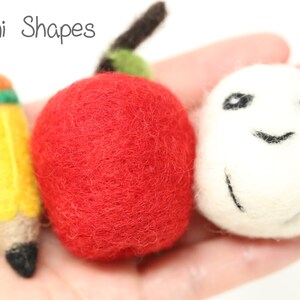 May include: A set of three felt mini shapes: a red apple, a yellow pencil with green and orange accents, and a white ball with a black smiley face.
