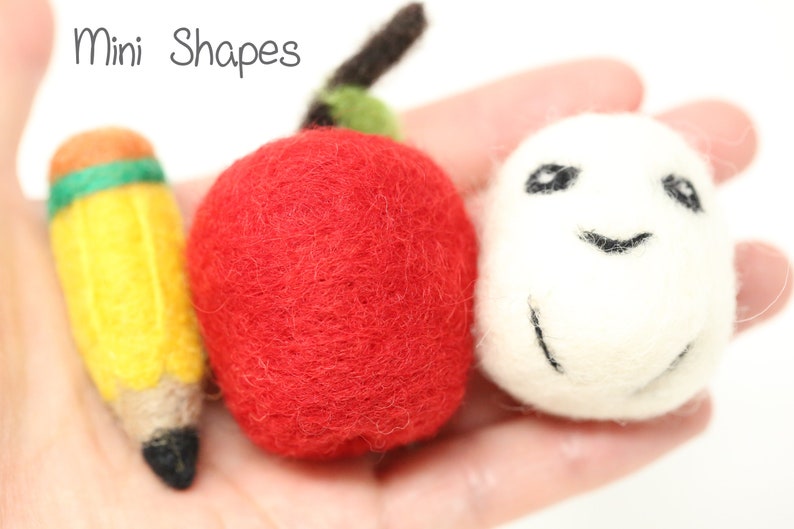 May include: A set of three felt mini shapes: a red apple, a yellow pencil with green and orange accents, and a white ball with a black smiley face.