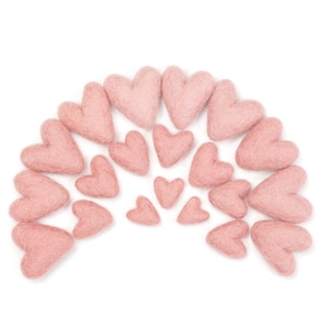 May include: A collection of pink felt hearts arranged in a semi-circle shape. The hearts are various sizes and are all a light shade of pink.