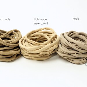 May include: Three spools of fabric hair ties in different shades of nude: dark nude, light nude (new color), and nude. The spools are arranged from left to right in order of darkness.