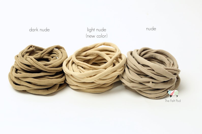 May include: Three spools of fabric hair ties in different shades of nude: dark nude, light nude (new color), and nude. The spools are arranged from left to right in order of darkness.