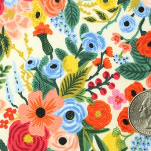 May include: Fabric with a floral pattern on a cream background. The design features a variety of flowers in red, orange, pink, blue, and yellow, with green foliage. A quarter coin is included for scale.