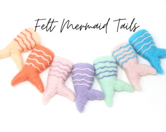 Könnte beinhalten: Sieben Filz-Meerjungfrauen-Schwänze in verschiedenen Pastellfarben mit weißen Streifen. Die Schwänze sind in einem Halbkreis auf weißem Hintergrund angeordnet. Der Text "Felt Mermaid Tails" steht über den Schwänzen.