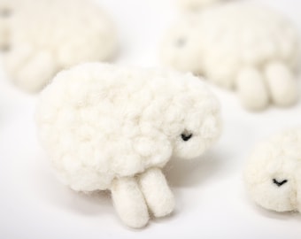 May include: A group of five white fluffy sheep made of felt. The sheep are all lying down with their heads resting on their front legs. The sheep have black eyes and noses.