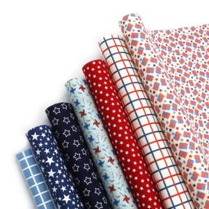 May include: A collection of rolled fabric featuring patriotic patterns. Designs include white stars on navy blue, red stars, blue pinwheels, and American flags. The fabrics are in shades of red, white, and blue.