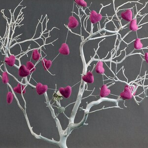 Puede incluir: Un &aacute;rbol de ramas blancas con corazones de fieltro rosa colgando de las ramas. Los corazones est&aacute;n enhebrados en un hilo blanco y est&aacute;n espaciados uniformemente.