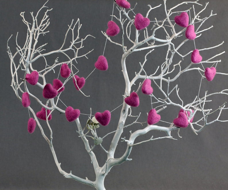 Puede incluir: Un &aacute;rbol de ramas blancas con corazones de fieltro rosa colgando de las ramas. Los corazones est&aacute;n enhebrados en un hilo blanco y est&aacute;n espaciados uniformemente.
