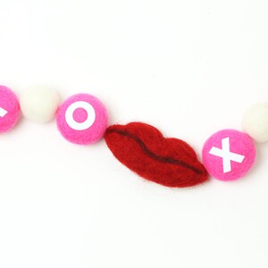 May include: A pink and white felt garland with red felt lips and white letters spelling "XO" for Valentine's Day decor.