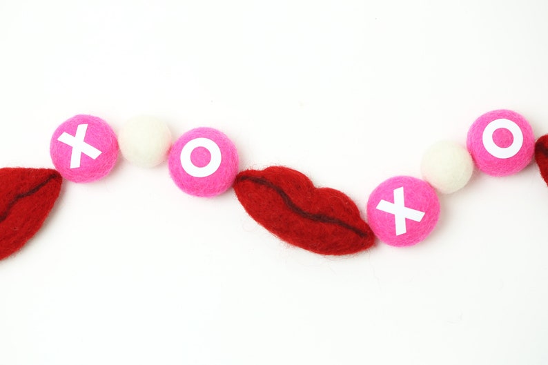 May include: A pink and white felt garland with red felt lips and white letters spelling "XO" for Valentine's Day decor.