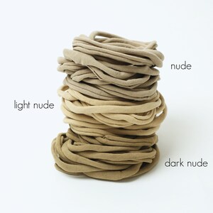 May include: A stack of nude hair ties in three shades: light nude, nude, and dark nude.