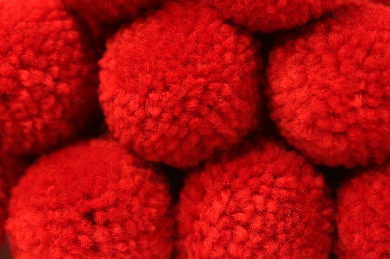 May include: Close-up of a group of red pom-poms. The pom-poms are soft and fluffy, and they are arranged in a random pattern.
